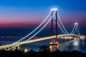 An awe-inspiring view of the 1915 Çanakkale Bridge, the world's tallest suspension bridge, majestically spanning the Dardanelles Strait in northwestern Turkey against a backdrop of clear blue skies.