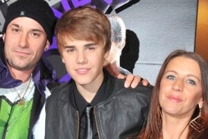 A family photo of Justin Bieber with his parents, Pattie Mallette and Jeremy Bieber, smiling at the camera.